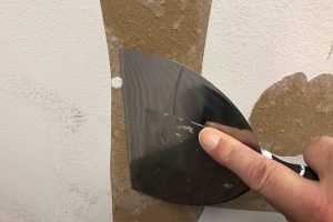 Preparation for torn drywall paper repair scraping the wall